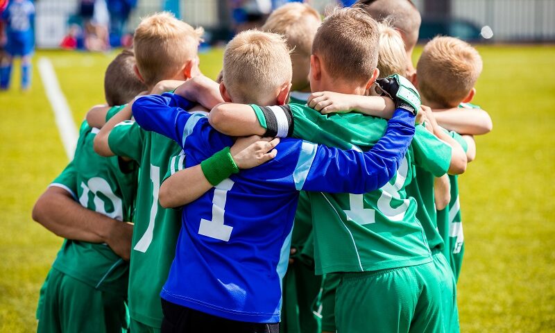 Group of kids playing football in a sunny day. Wearing green and Blue Jersey.