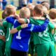 Group of kids playing football in a sunny day. Wearing green and Blue Jersey.