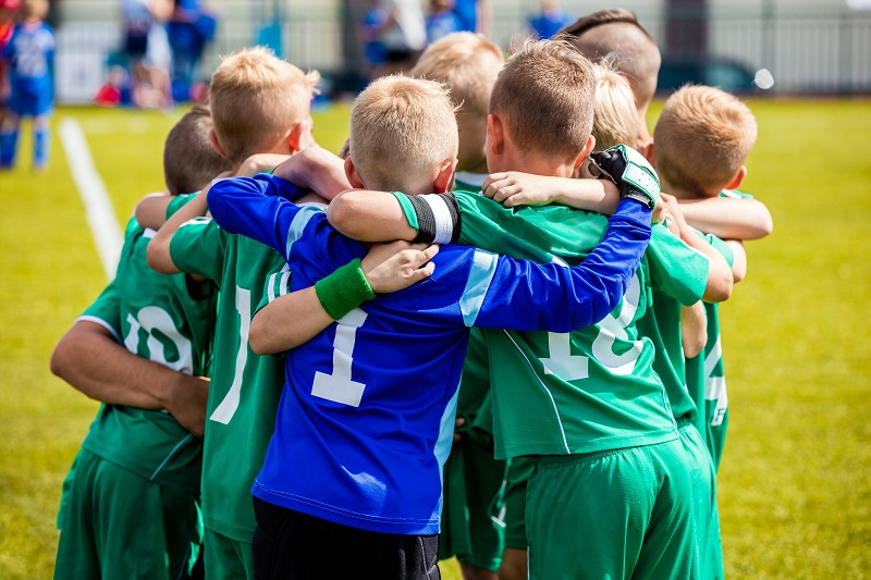 Group of kids playing football in a sunny day. Wearing green and Blue Jersey.